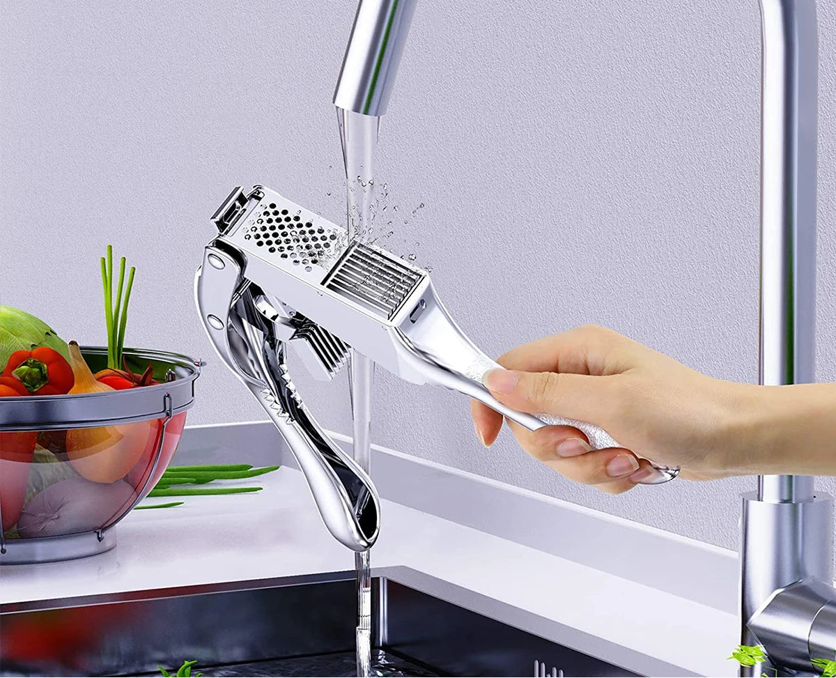 Hand using a garlic press under running water with text 'Easy to Clean' and 'Rinse directly with water or wash in the dishwasher'.